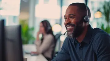 Ein dunkelhäutiger Mann arbeitet im Kundenservice am Telefon und lächelt